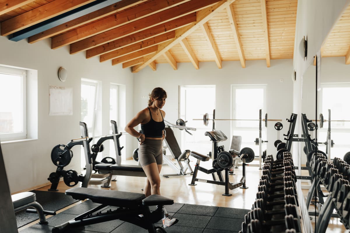Eine Sportlerin im Freihantelbereich des TNT Fitness zwischen Hantelbänken und Kurzhantelregal